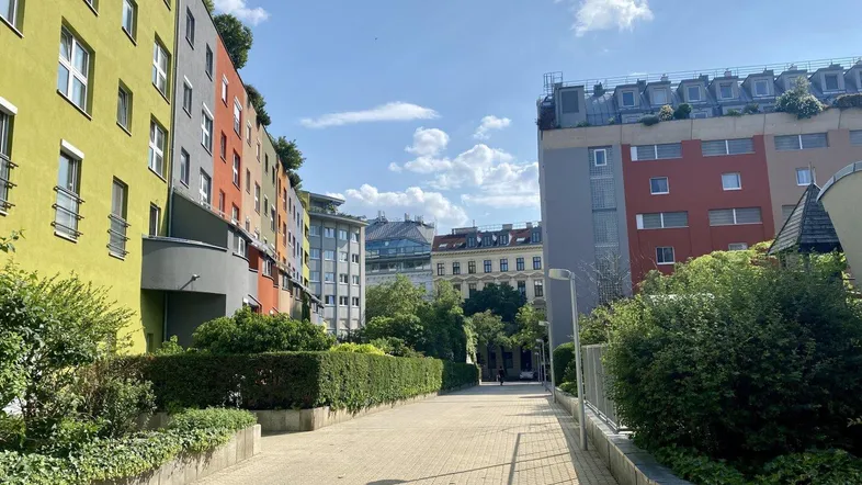 Moderne Wohngebäude mit farbigen Fassaden und begrünten Dächern entlang eines gepflasterten Weges in der Stadt.