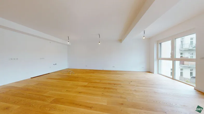 Helles, leeres Wohnzimmer mit Holzboden und großen Fenstern, bereit für die individuelle Gestaltung.