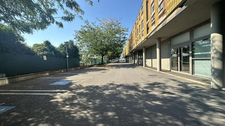 Langer Gehweg entlang der modernen Gebäudefassade mit Parkplätzen und Bäumen an einem sonnigen Tag.