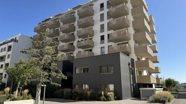 Modernes Mehrfamilienhaus mit zahlreichen Balkonen und gepflegter Außenanlage unter blauem Himmel.
