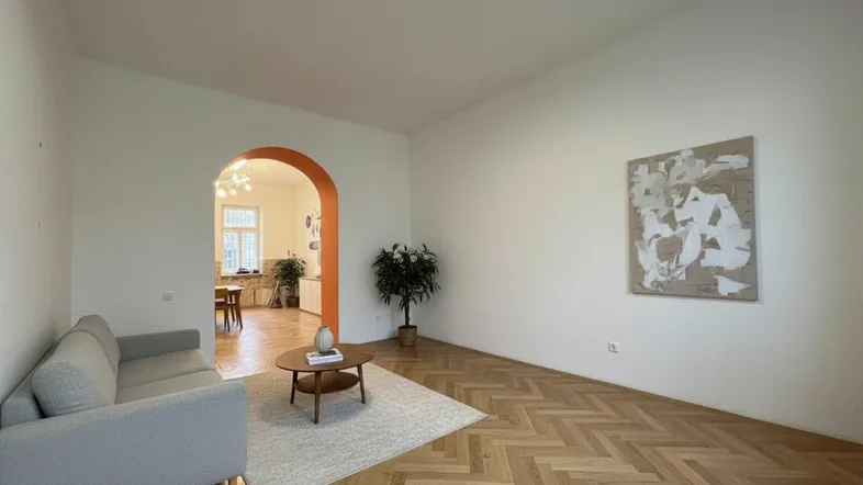 Helles Wohnzimmer mit Fischgrätparkettboden und einem Durchgang zu einem weiteren Raum.
