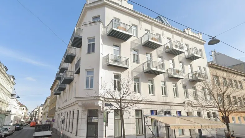 Historisches Eckgebäude mit mehreren Balkonen und klassischer Architektur in einer städtischen Umgebung.