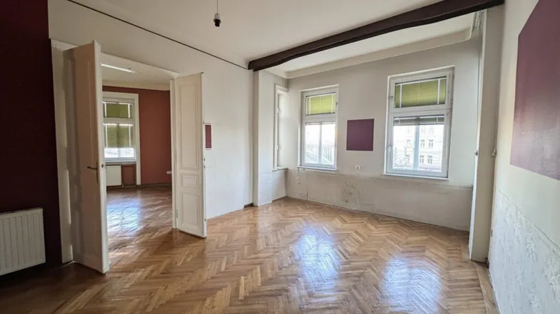 Geräumiges Zimmer mit Fischgrätparkett, hohen Decken und großen Fenstern, bereit zur individuellen Gestaltung.