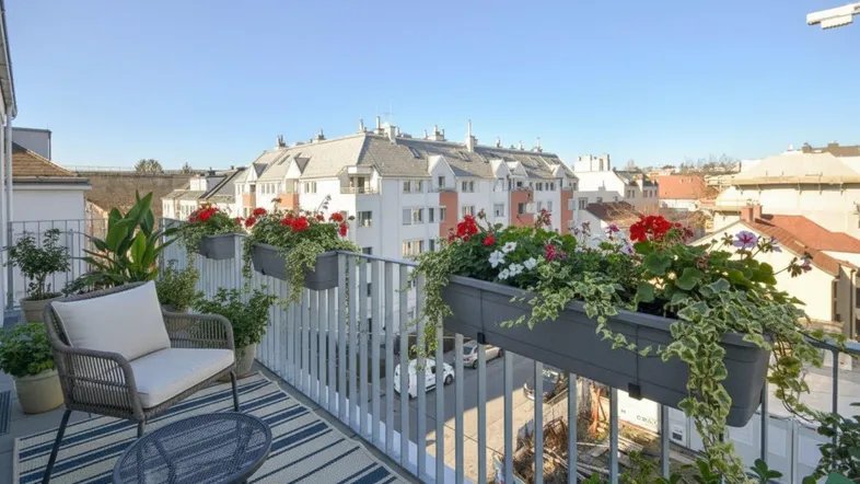 Möblierter Balkon mit Blumenkästen und Blick auf die umliegenden Gebäude in der Stadt.