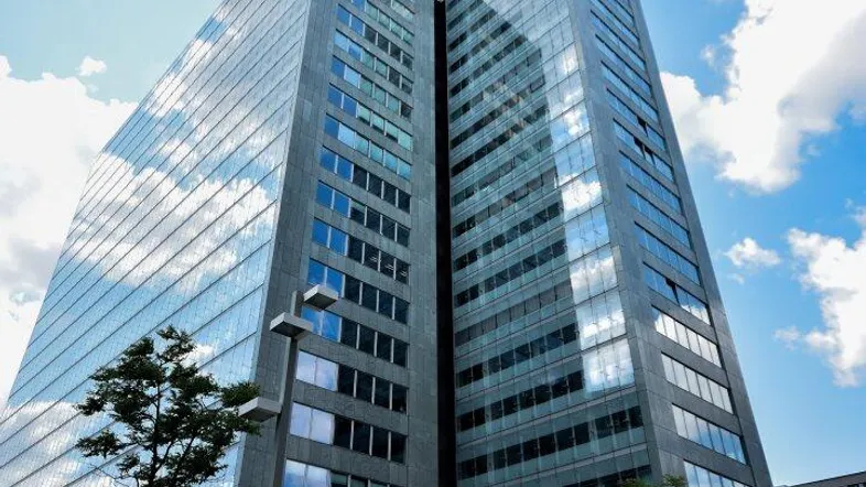 Beeindruckendes modernes Hochhaus mit Glasfassade unter einem dynamischen Himmel mit Wolken.