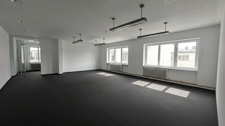 Geräumiger Büroraum mit Teppichboden, großen Fenstern und natürlichem Lichteinfall.
