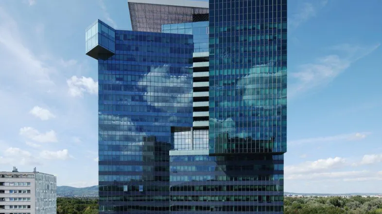 Modernes Hochhaus mit blauer Glasfassade und reflektierenden Wolken unter blauem Himmel.
