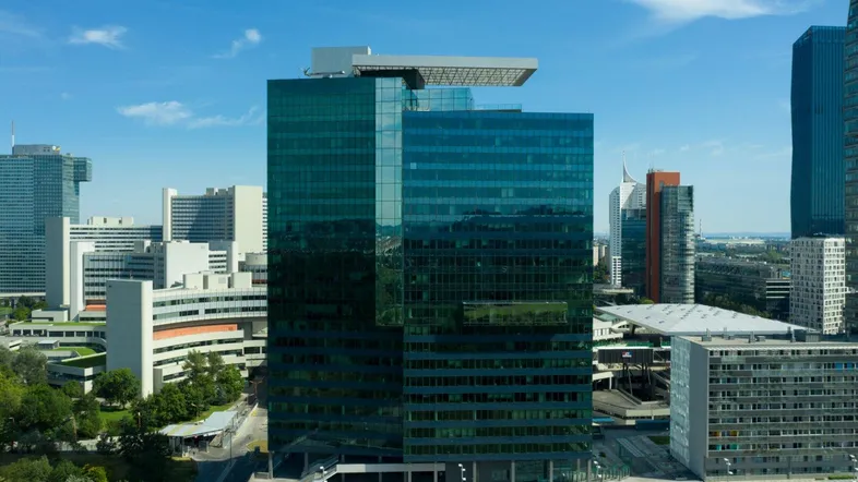 Modernes Hochhaus mit blauer Glasfassade in einer städtischen Umgebung unter blauem Himmel.