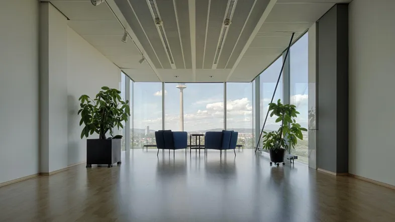 Moderne Lounge mit großen Fenstern, Holzboden und bequemen blauen Sesseln, bietet eine weite Aussicht.