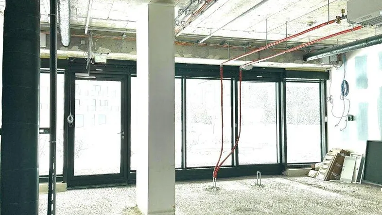 Unfertiger Innenraum mit sichtbaren Leitungen, Betonboden und großen Fenstern, bereit für den Ausbau.