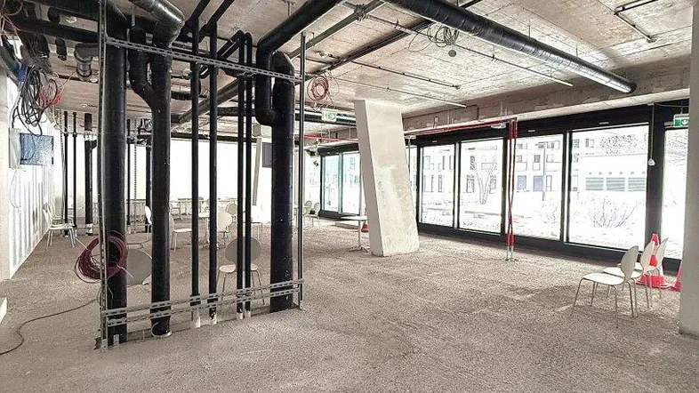 Großer, unfertiger Gewerberaum mit freiliegenden Rohren, Betonboden und großen Fenstern, bereit für den Ausbau.