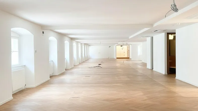 Großer, heller Büroraum mit Fischgrätparkett, weißen Wänden und vielen Fenstern, bereit für die Gestaltung.