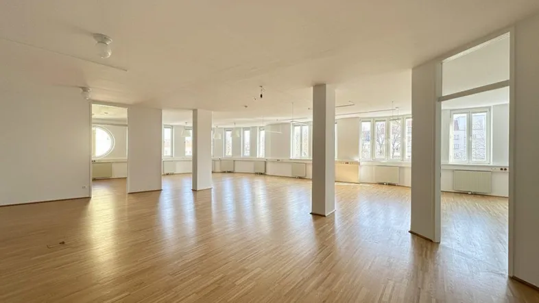 Großer, heller Büroraum mit vielen Fenstern und Holzboden, ideal für offene Arbeitsbereiche.