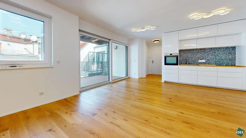 Helles, offenes Wohnzimmer mit integrierter moderner Küche, Holzboden und Zugang zum Balkon.