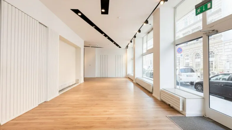 Heller, leerer Ladenbereich mit großen Schaufenstern, Holzboden und moderner Deckenbeleuchtung.