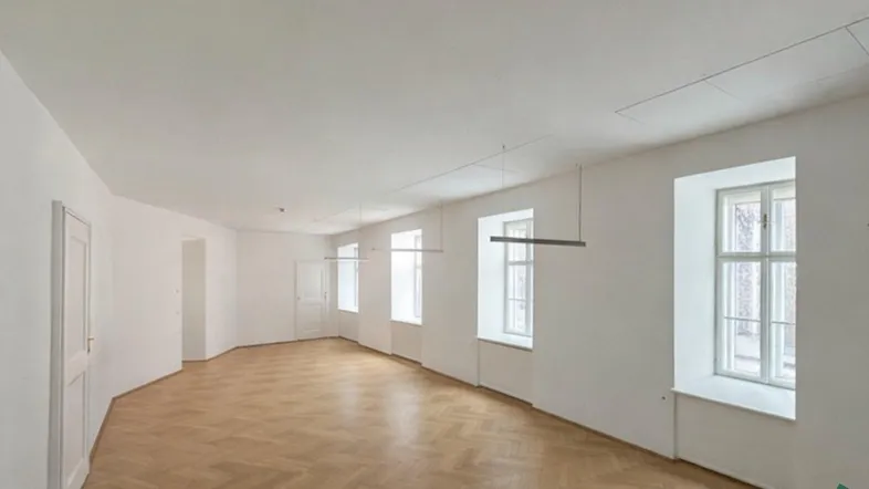 Geräumiger, heller Raum mit Fischgrätparkettboden und mehreren Fenstern, ideal für Wohn- oder Büronutzung.