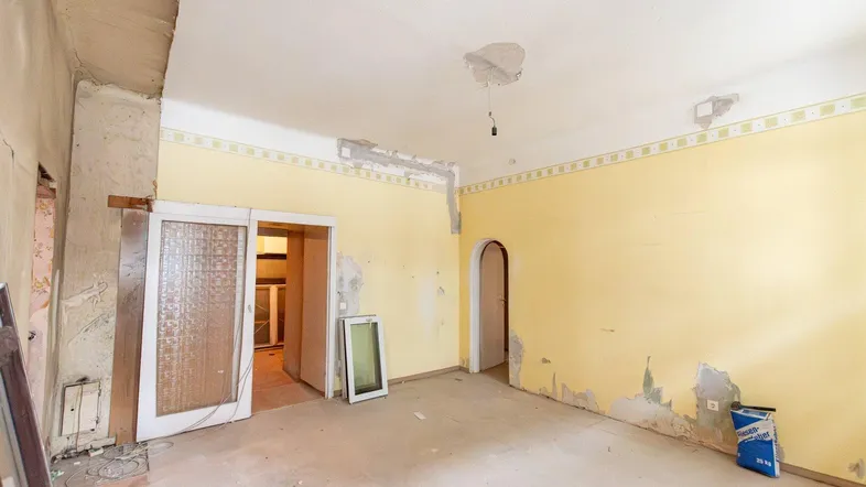 Renovierungsbedürftiger Raum mit gelben Wänden, alten Türen und sichtbaren Baumaterialien.