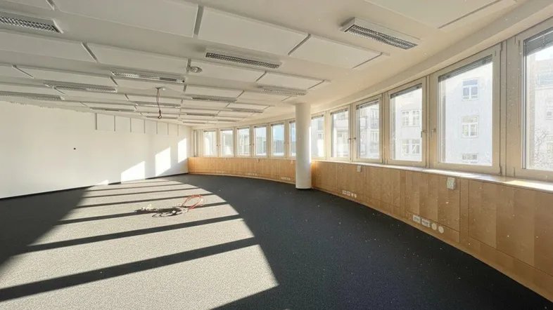 Großes, helles Büro mit Teppichboden, vielen Fenstern und Akustikdeckenplatten, ideal für offene Arbeitsbereiche.