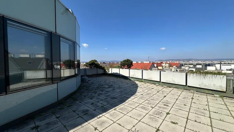 Große geflieste Dachterrasse mit weitem Blick über die Stadt und angrenzendem modernen Gebäude.
