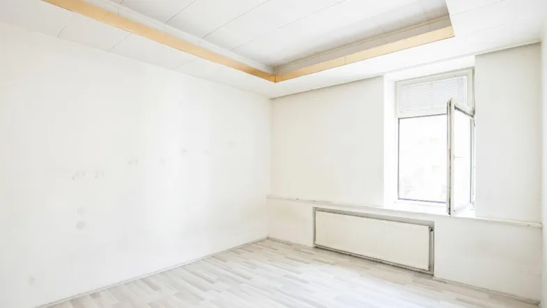 Helles, leeres Zimmer mit Laminatboden und einem Fenster, bereit zur individuellen Gestaltung.