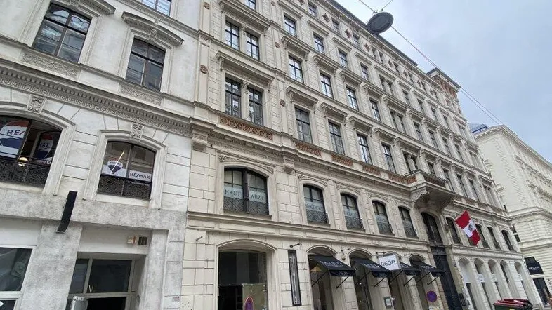 Historisches Gebäude mit klassischer Fassade und großen Fenstern an einer belebten Straße unter bewölktem Himmel.