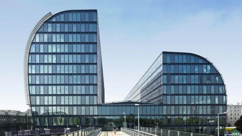 Modernes Gebäude mit geschwungener Glasfassade und markanter Architektur unter blauem Himmel.