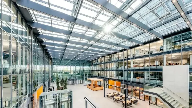 Großzügiges, lichtdurchflutetes Atrium mit Glasdach, mehreren Büroetagen und Sitzbereichen.