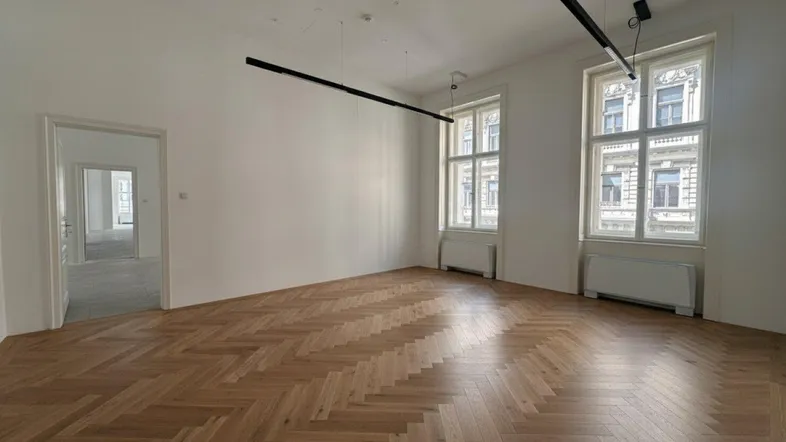 Leerer Büroraum mit Fischgrätparkett, hohen Decken und großen Fenstern, bereit zur Einrichtung.
