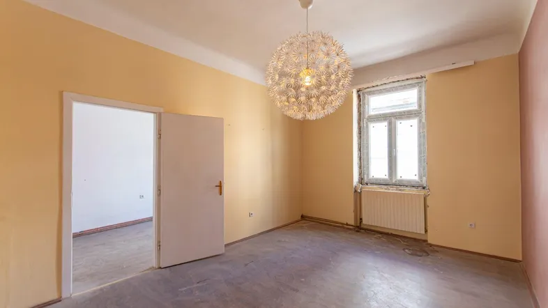 Unmöblierter Raum mit gelben Wänden, einem Fenster und einer auffälligen Deckenleuchte.