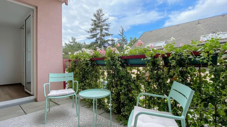 Gemütlicher Balkon mit Sitzgelegenheiten und üppiger Bepflanzung unter blauem Himmel.
