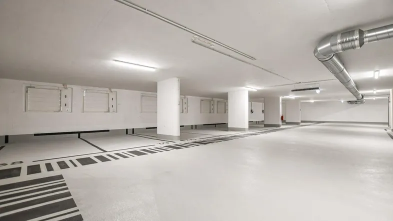 Geräumige Tiefgarage mit markierten Stellplätzen und sichtbaren Lüftungsrohren, gut beleuchtet.