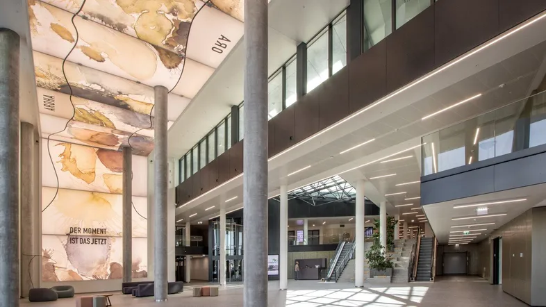 Großzügige, moderne Lobby mit hohen Decken, künstlerischer Deckengestaltung und viel Tageslicht.