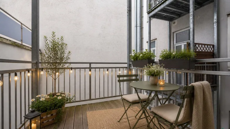 Gemütlicher Balkon mit Holzboden, Sitzgelegenheiten und stimmungsvoller Lichterkette.