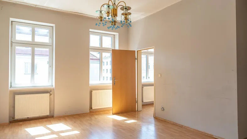 Helles Zimmer mit Holzboden, zwei Fenstern und einem Kronleuchter, bereit zur individuellen Gestaltung.