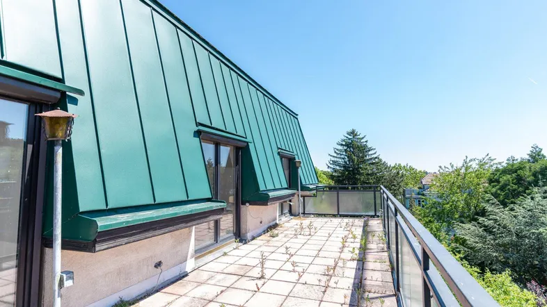 Große Dachterrasse mit Fliesenboden, Glasgeländer und weitem Blick ins Grüne.