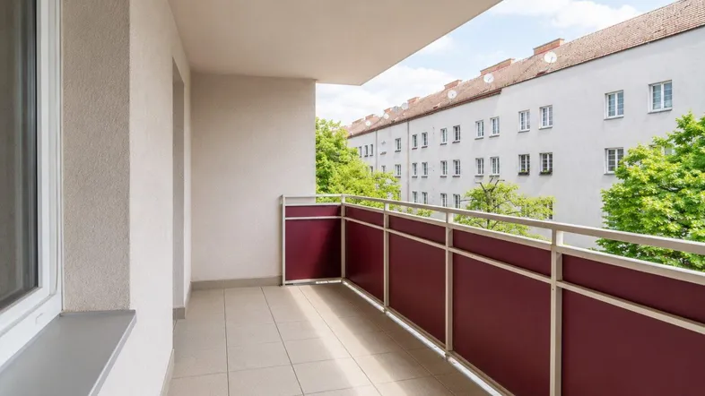 Geräumiger Balkon mit Fliesenboden und Blick auf die umliegenden Gebäude und Bäume.