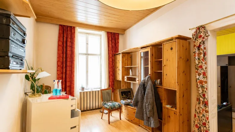 Gemütliches Wohnzimmer mit Holzdecke, Laminatboden und traditionellen Holzmöbeln, hell beleuchtet.