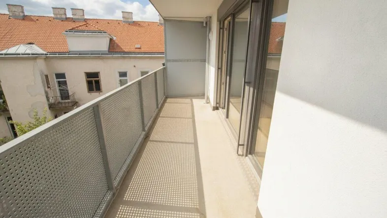 Langer Balkon mit modernem Metallgeländer und Blick auf die umliegenden Gebäude unter blauem Himmel.