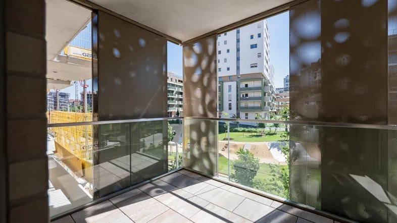 Heller Balkon mit Fliesenboden, Glasgeländer und Blick auf die umliegenden Gebäude und Grünflächen.