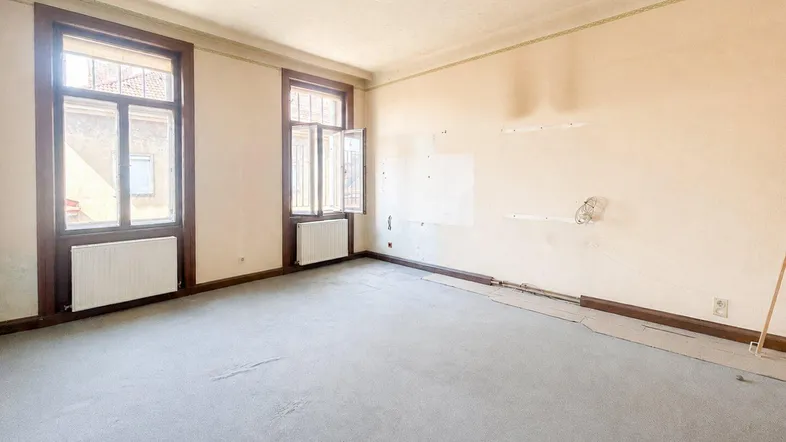 Geräumiges, unmöbliertes Wohnzimmer mit Teppichboden und zwei großen Fenstern, bereit zur Renovierung.