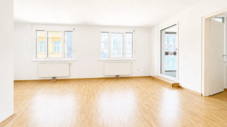 Helles, leeres Zimmer mit Parkettboden und Zugang zu einem Balkon, ideal als Wohnzimmer.