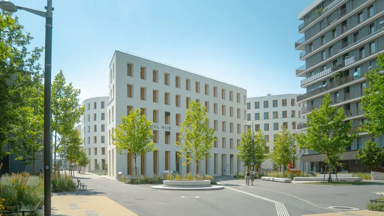 Moderne weiße Gebäude mit vielen Fenstern und grüner Umgebung unter blauem Himmel.