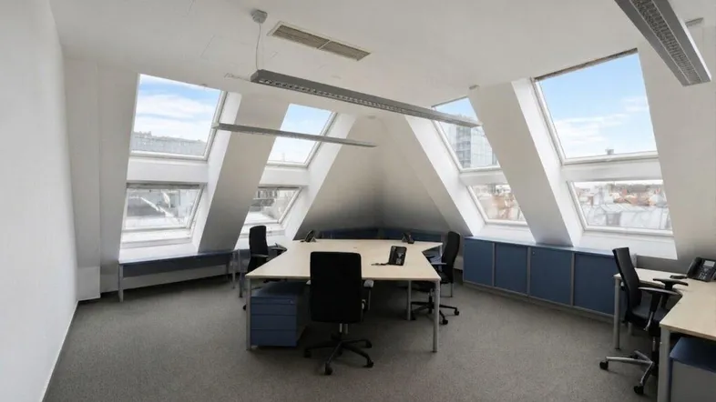 Helles Dachgeschossbüro mit mehreren Arbeitsplätzen, Teppichboden und großen Dachfenstern.