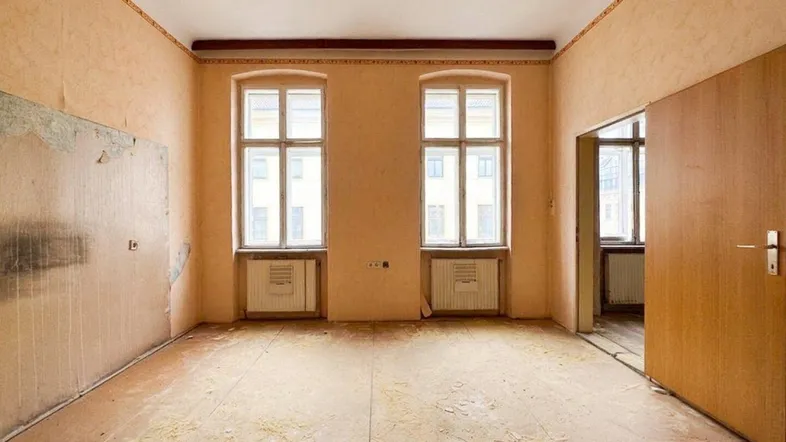 Geräumiger Raum in sanierungsbedürftigem Zustand mit zwei Fenstern und abgenutztem Boden.