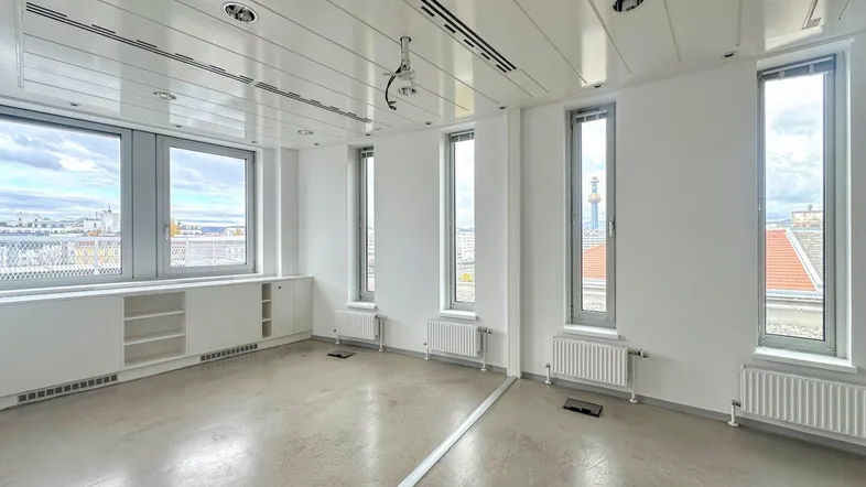 Heller, leerer Büroraum mit großen Fenstern, die einen weiten Blick über die Stadt bieten.