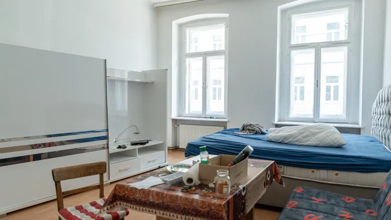 Helles Schlafzimmer mit Bett, Tisch und Schrank, ausgestattet mit zwei großen Fenstern.