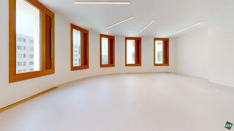 Heller, leerer Raum mit mehreren Holzfenstern und modernen Deckenleuchten, ideal für Büronutzung.