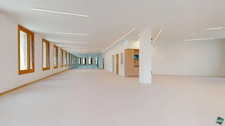 Geräumiger, heller Gewerberaum mit vielen Fenstern, einer integrierten Teeküche und modernen Leuchten.