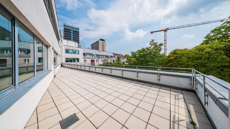Geräumige Dachterrasse mit Fliesenboden und Blick auf die umliegende Stadtlandschaft und einen Kran.