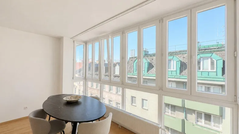 Heller Essbereich mit modernem Tisch und Stühlen, umgeben von großen Fenstern mit Stadtblick.
